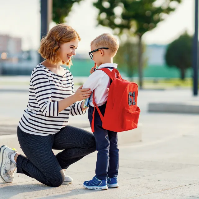Parent kneeling to hug a young student wearing a red backpack